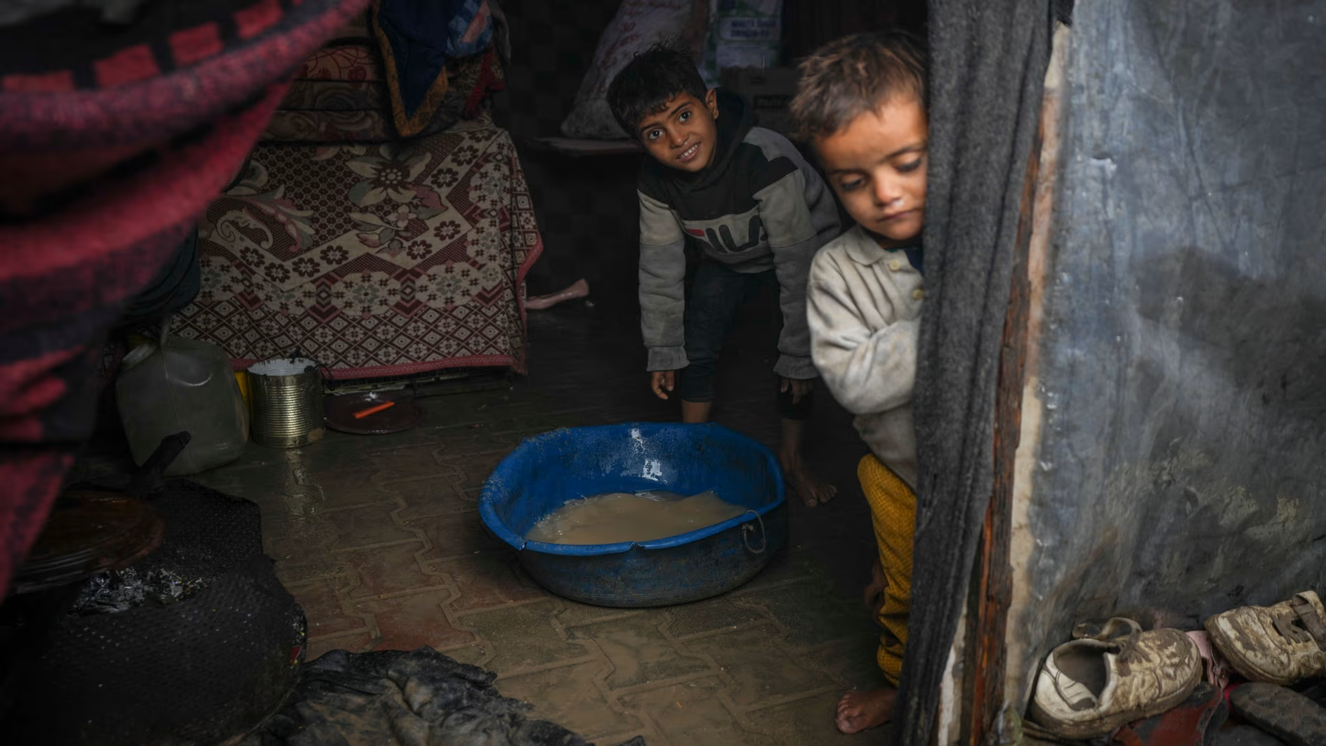 Brothers Belal, 5, and Mohammed Hamad, 7, collect water from their flooded family tent at a refugee tent camp for displaced Palestinians in Deir al-Balah, central Gaza Strip.